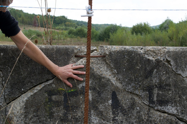 Performance im Freien, Hand auf Steinmauer, im Hintergrund Landschaft