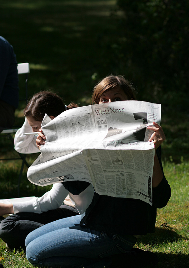 Eine Studentin hält eine Tageszeitung vor ihr Gesicht.