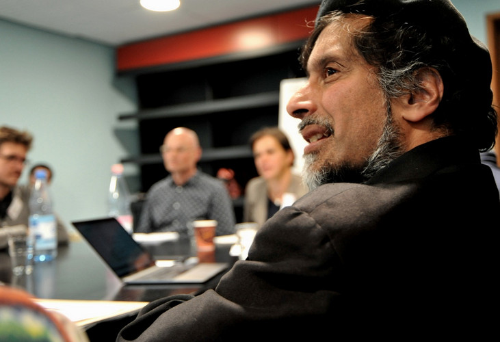 Person speaks in front of group around table.