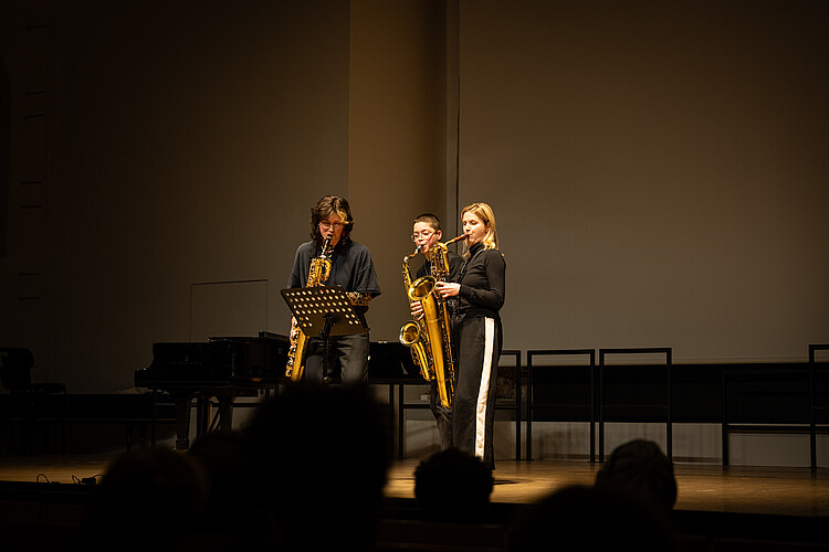 Drei Saxofonistinnen spielen, sich zugewandt, auf der Bühne.