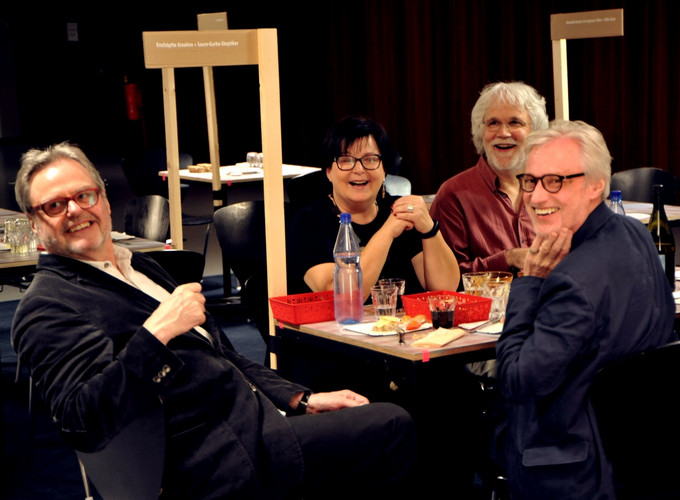 Four people laughing torwards camera, sitting at a table within an installation