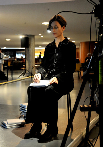 Sitting Person notes something into a Notebook in front of a Video Installation.