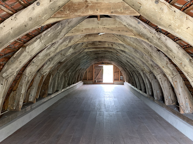 Blick in einen alten Dachstuhl. Holzgedübelte Sparren und Streben bilden Rundbögen und verleihen dem Raum den Charakter eines Tonnengewölbes.