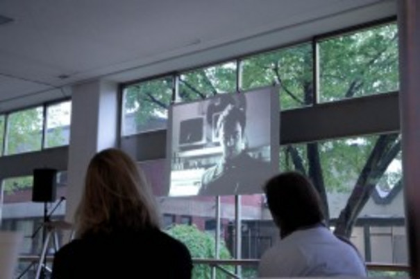 Dokumentation einer Ausstellung: zwei Besucher blicken auf Videoinstallation