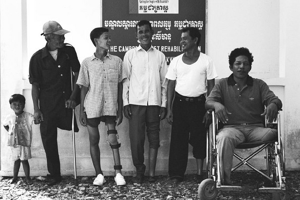 Six males with different leg related disabilities in a row smiling at each other or the camera.