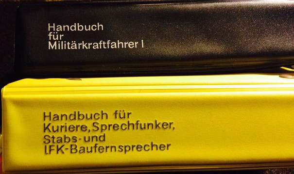 Schwarzer Buchrücken vom &quot;Handbuch für Militärkraftfahrer I&quot; auf gelbem Buchrücken vom &quot;Handbuch für Kuriere, Sprechfunker, Stabs- und IFK-Baufernsprecher&quot;.