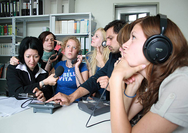 Eine Gruppe Studenten sitzt an einem Tisch und hört Radio.