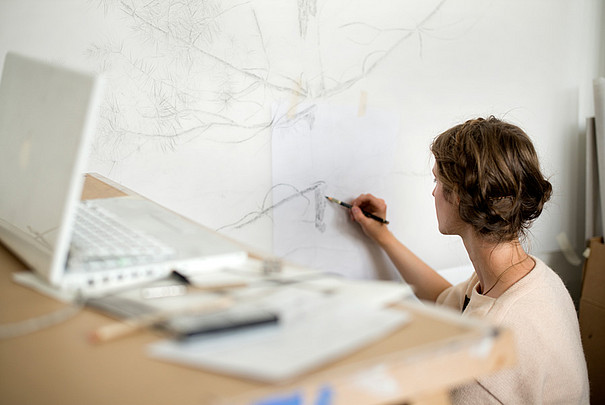 Eine junge Frau, die an einer weissen Leinwand skizziert.